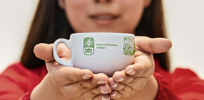 White mug with “Cafés del Perú” logo, held by a woman's hands, symbolizing the sectorial brands.