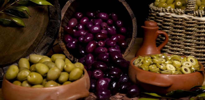 Botella de aceite de oliva virgen extra y aceitunas verdes frescas sobre tela de saco y tabla de madera, representando la calidad de los productos peruanos del sur