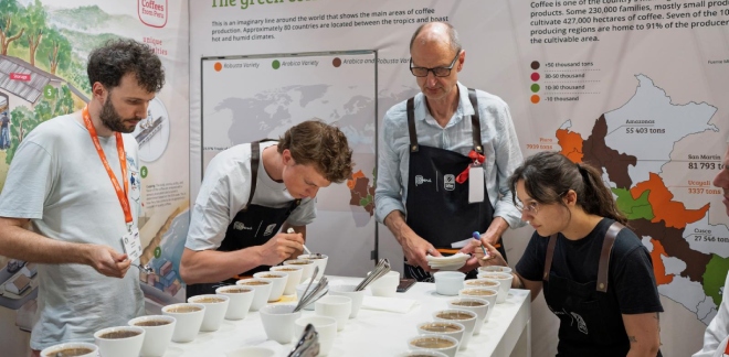 Tres personas catando o evaluando varias tazas de café en la sala de cata del stand peruano en la World of Coffee.