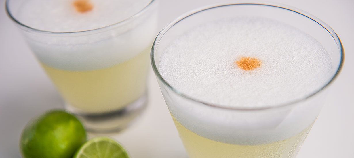 Pisco Sour peruano acompañado de limas frescas, mostrando la presentación clásica de este cóctel tradicional sudamericano.