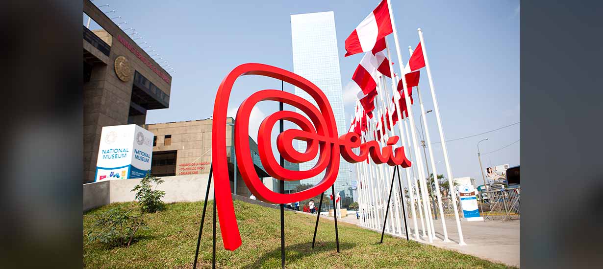 An emblematic sculpture of the Peru brand located in front of the National Museum of Lima, accompanied by Peruvian flags and modern buildings.